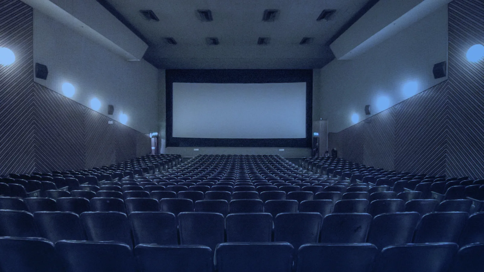 Sala de cine vacía con filas de butacas frente a una pantalla grande