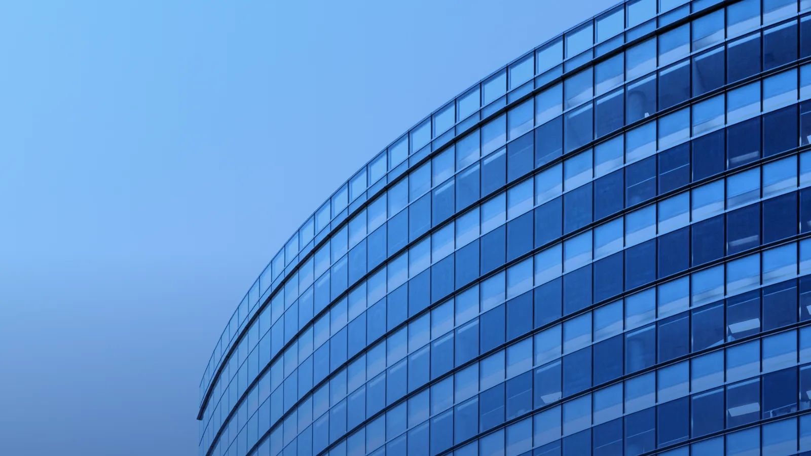 Fachada curva de vidrio de un edificio de oficinas bajo cielo azul