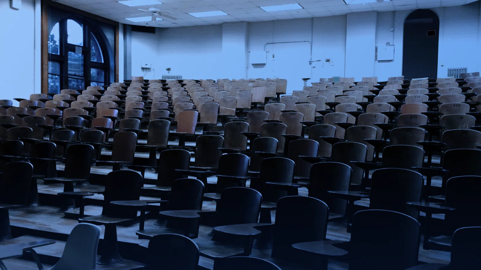 Aula universitaria vacía con sillas de madera y grandes ventanales