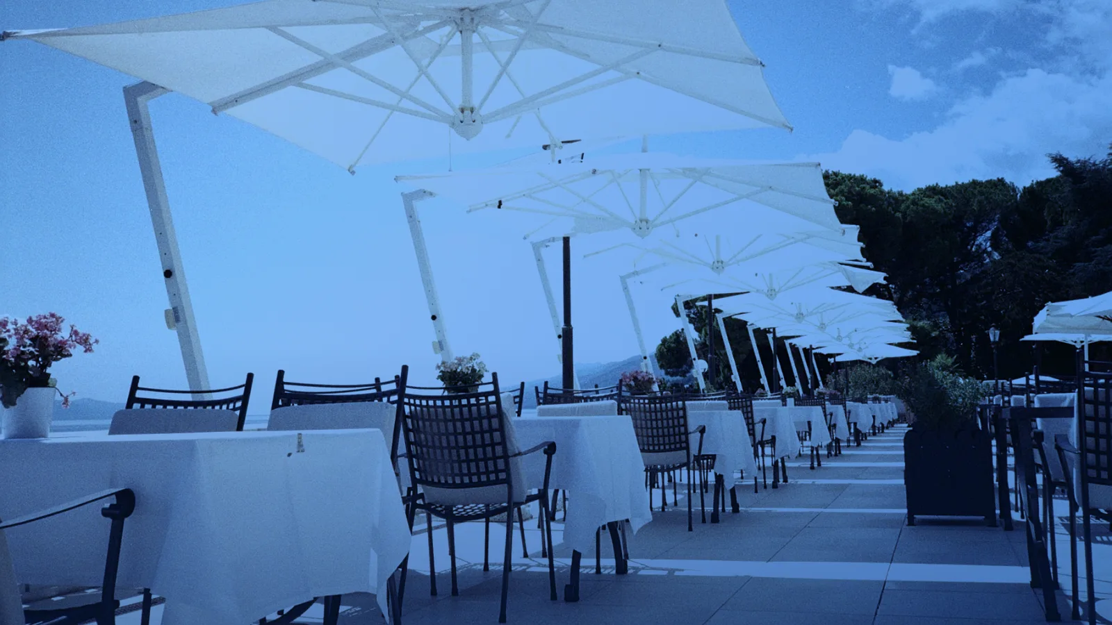 Terraza de restaurante junto al mar con mesas bajo sombrillas blancas