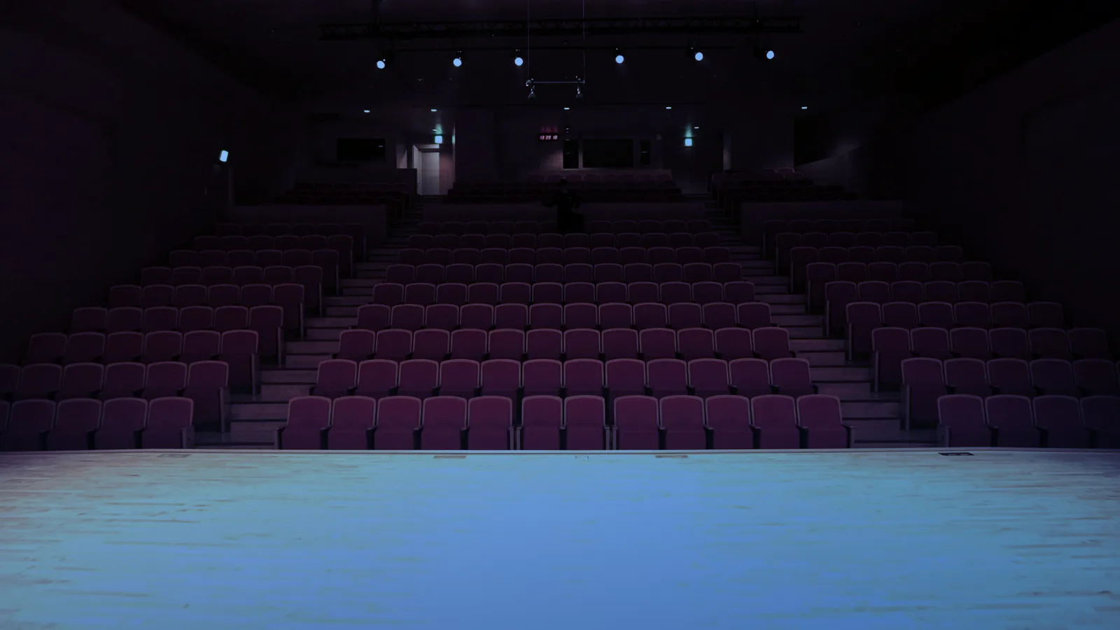 Teatro vacío con butacas rojas y el escenario iluminado