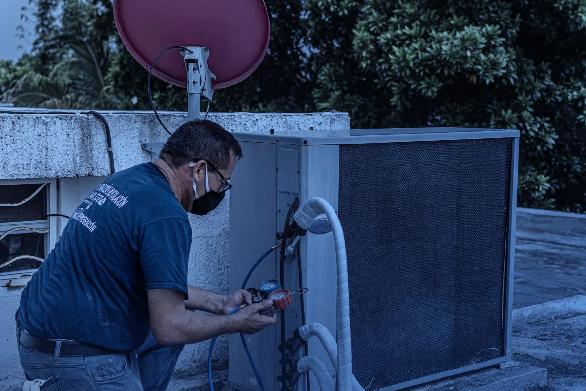 Técnico de aire acondicionado con mascarilla revisando una unidad exterior